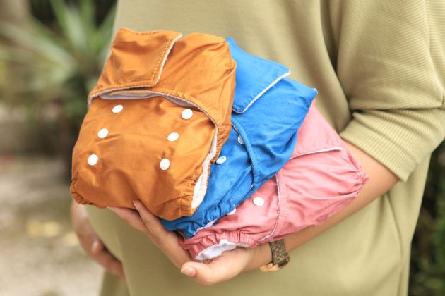 A closeup photo of someone holding three brightly coloured reusable diapers, or nappies.