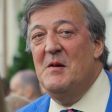 Photo of Stephen Fry. The photo is close-up, and he is wearing a blue suit jacket and a white shirt.