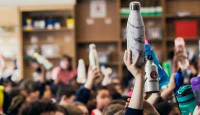 Reusable water bottles being held up by a class of children who are learning about plastic pollution solutions.