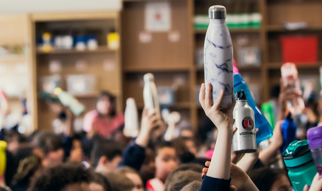 Reusable water bottles being held up by a class of children who are learning about plastic pollution solutions.