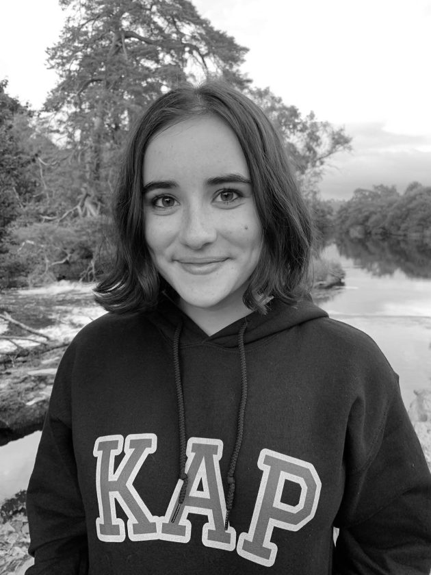 Profile photo for Amy Meek, Youth Action Lead at Common Seas. Amy wears a hooded jumper with 'KAP' (Kids Against Plastic) embroidered across the chest. She is smiling at the camera. Photo is in greyscale