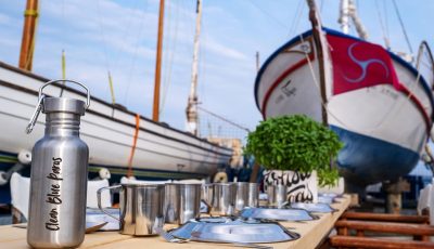Photo down a long table of reusable bottles and campaign materials, with a sailing boat in the background