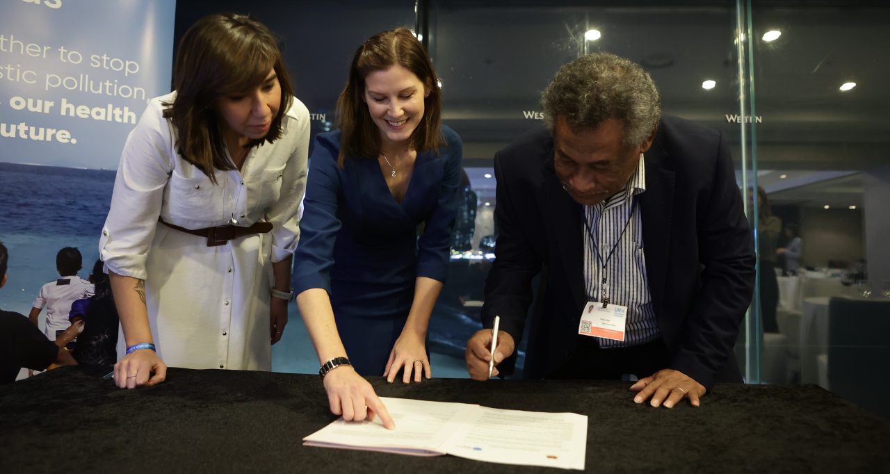 Veari Kula of Papua New Guinea signs an MOU at an event at INC5 in Busan. Thais Vojvodic slides at the camera and Charlotte Davies points at the document.c