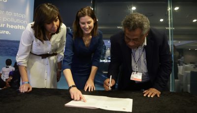 Veari Kula of Papua New Guinea signs an MOU at an event at INC5 in Busan. Thais Vojvodic slides at the camera and Charlotte Davies points at the document.c