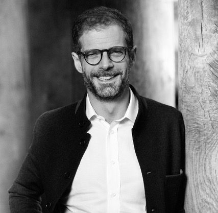 Profile photo for Adonis Lemos, Executive advisor at Common Seas. He wears a dark blazer and white shirts, plus glasses. He smiles at the screen. Photo is in greyscale.