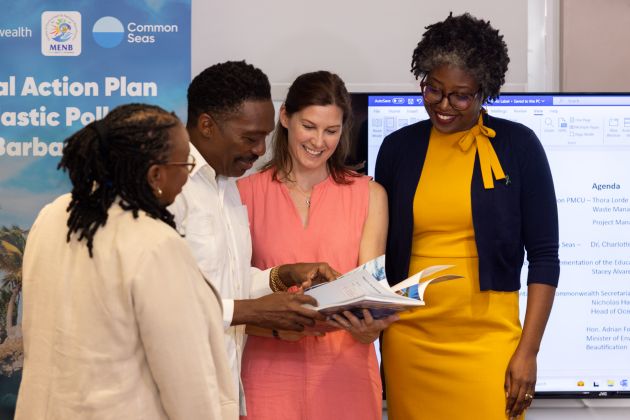 Four people looking at the National Action Plan on Plastic Pollution in Barbados. In the centre, Dr Charlotte Davies and Hon Adrian Forde are leafing through the report.