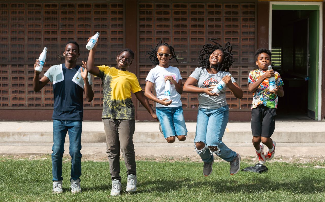 Five school children in Barbados in a line, facing the camera and jumping in the air.