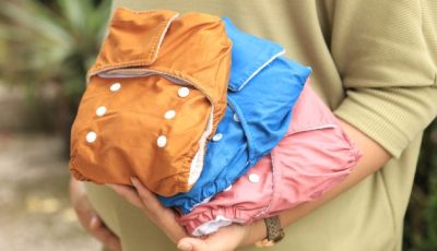 A closeup photo of someone holding three brightly coloured reusable diapers, or nappies.