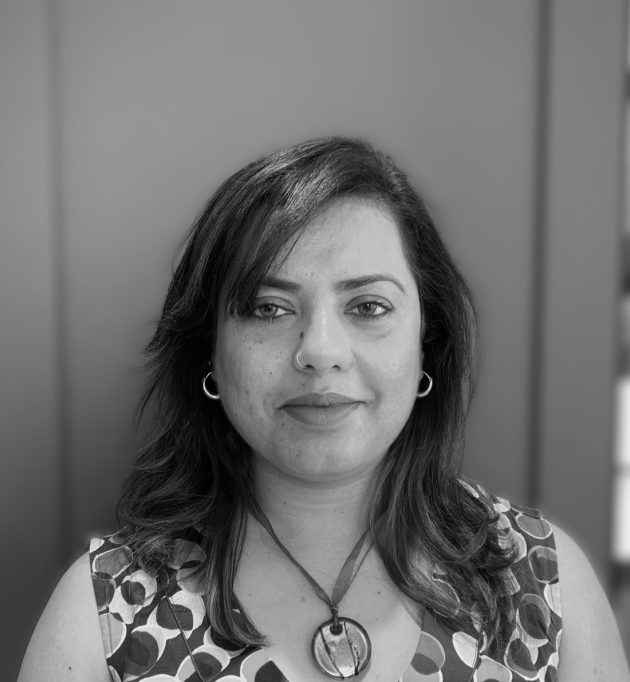 Profile photo of Faryal Gohar, Project Manager at Common Seas. Faryal wears a short-sleeved patterned blouse and a pendant necklace, and is smiling at the camera. Photo is in greyscale.