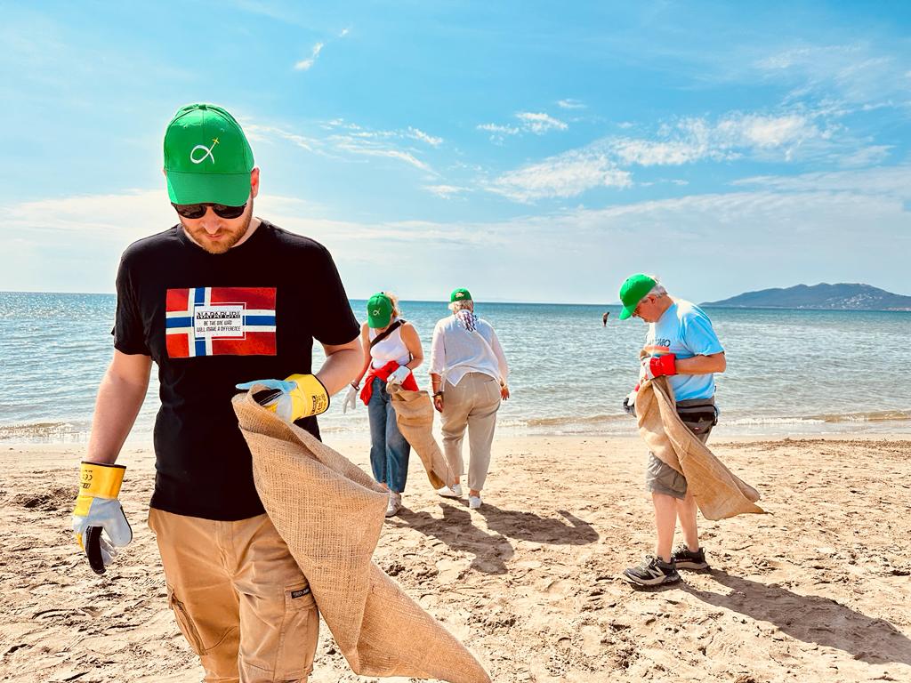 A beach clean-up in Greece, with a figure walking towards the camera holding a sack.
