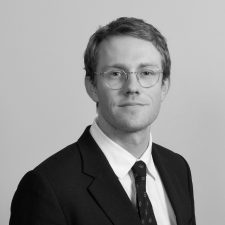 Profile photo of Patrick Cumming, Data Modelling Lead at Common Seas. Patrick wears a dark blazer, white shirt and dark tie, with glasses. He is looking at the camera slightly smiling. Photo is in greyscale.