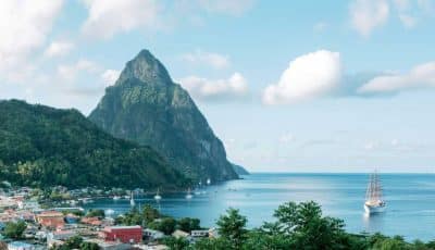 Photo along the coast of Saint Lucia towards the mountains, known as The Pitons. The sky and sea are blue, with dark green rainforest in the foreground.