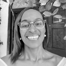 Profile photo of Stacey Alvarez de la Campa. Stacey wears a striped collared shift and glasses. She smiles at the camera. Photo is in greyscale