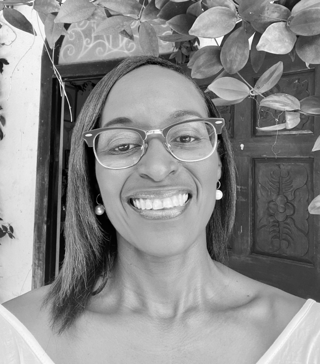 Profile photo of Stacey Alvarez de la Campa. Stacey wears a striped collared shift and glasses. She smiles at the camera. Photo is in greyscale